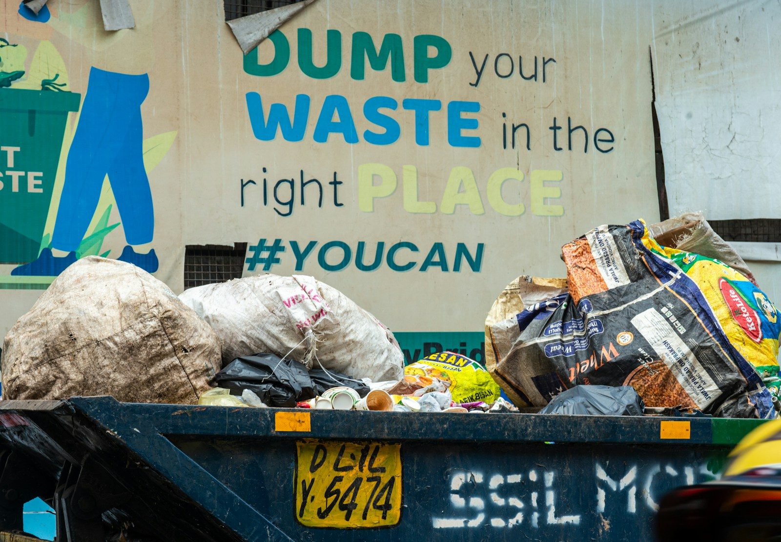 Overflowing dumpster with bags of trash and signage.